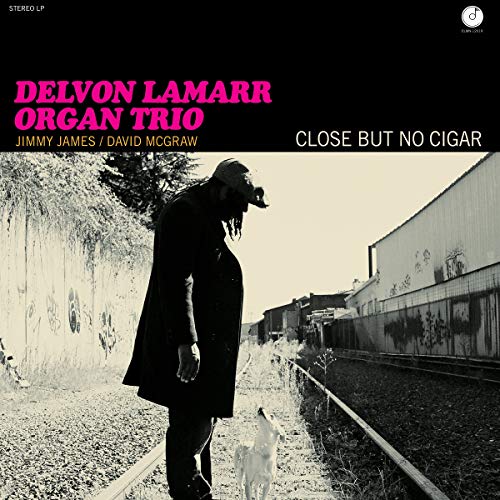 Vinyl record cover: Delvon Lamar Organ Trio, man with dog, industrial background.