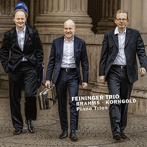 Three formally dressed musicians, the Feininger Trio, walking towards the viewer.