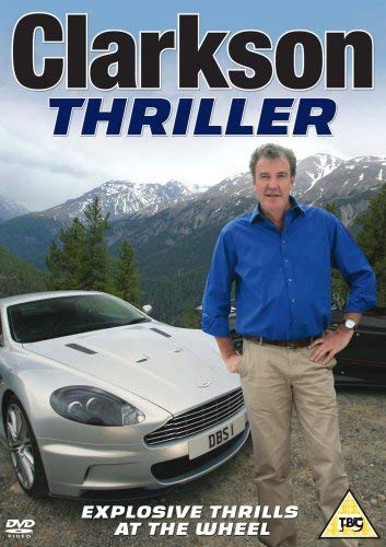 "Jeremy Clarkson stands beside a silver Aston Martin car with mountains in the background."