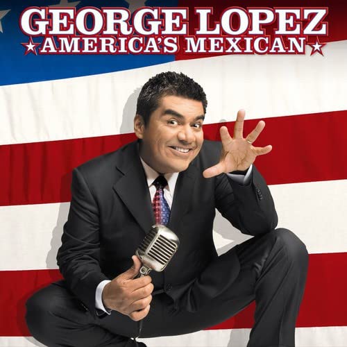 George Lopez in a suit holding a vintage microphone, American flag backdrop.