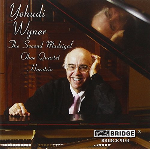 Yehudi Wyner sits at a grand piano, smiling, in a wood-paneled room.