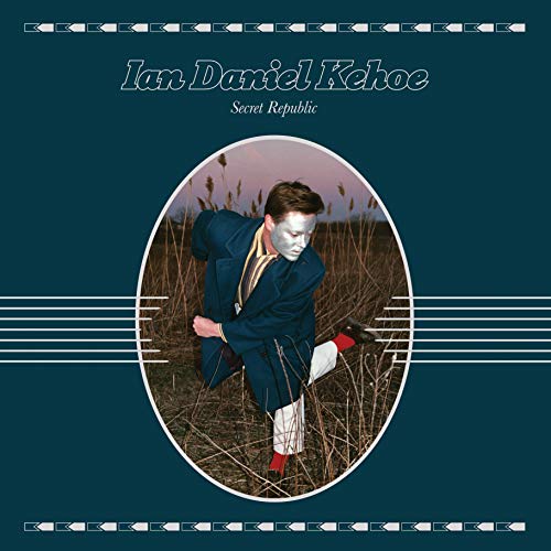 "Album cover with man in dark coat and white pants in tall grass."