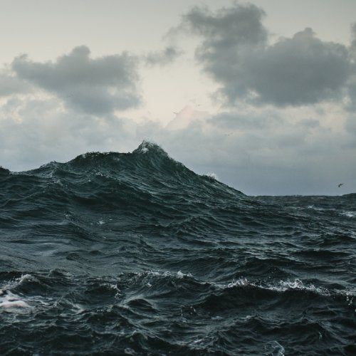 Dark, stormy ocean waves under a cloudy, bright sky.