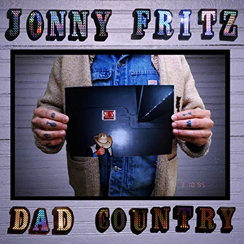 Man in cardigan and denim overalls holding a vinyl record sleeve with cartoon character.