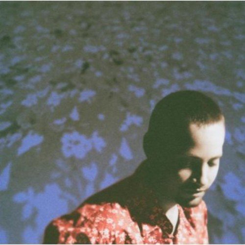 Man in a red shirt with a white pattern, looking down, against a blue background.
