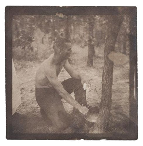 A sepia-toned photograph of a shirtless man chopping wood in a forest.
