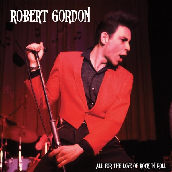 Robert Gordon in red suit singing into a microphone onstage.