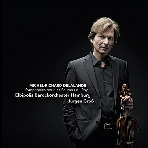 A man in a suit holding a violin against a black background.