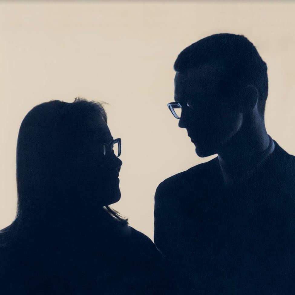 Silhouettes of a man and woman facing each other, wearing glasses.