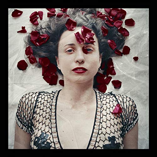 A woman wearing a beaded mesh top lies surrounded by scattered red rose petals.