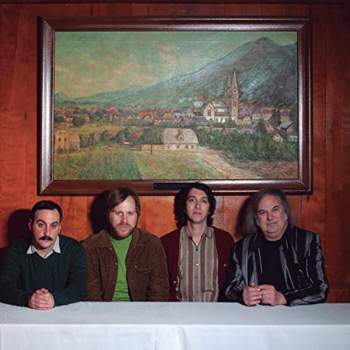 Four men pose below a landscape painting in ornate frame.
