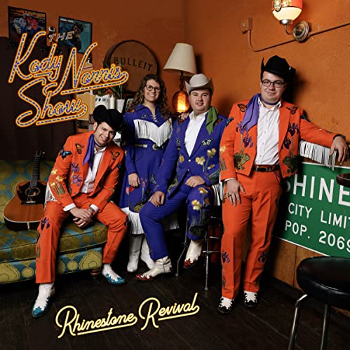 Four musicians in colorful, rhinestone-embellished suits pose in a warmly lit room.