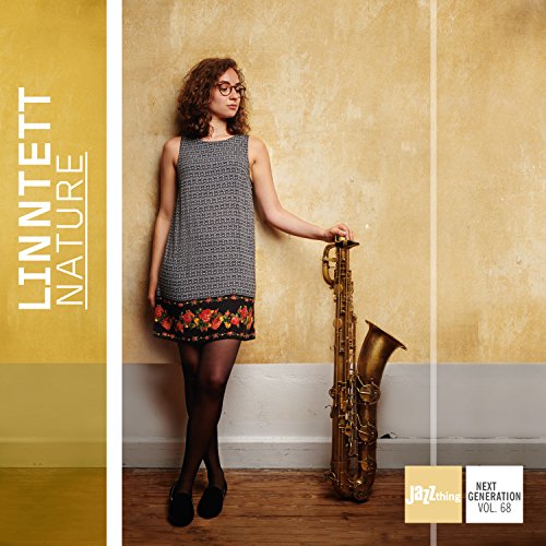 Woman in patterned dress and tights holding a saxophone against a beige wall.