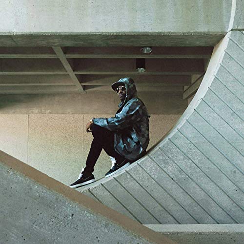 A man sits on a concrete ledge, wearing a blue jacket and black pants.