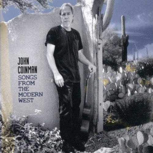 Album cover with man holding guitar, standing by wall, in desert landscape.
