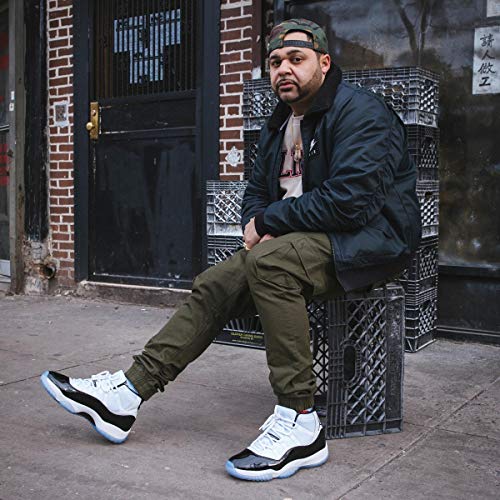 "Man sitting on crate, wearing jacket, hat, and sneakers, outdoors."