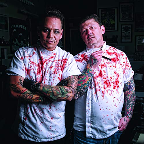 Two tattooed men in blood-splattered shirts pose in a shop interior.
