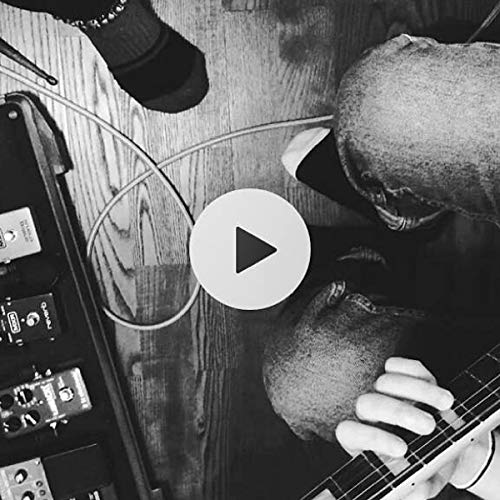 Black and white image of a man playing an electric guitar with effects pedals nearby.