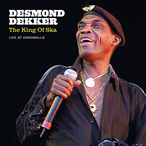 Desmond Dekker portrait, smiling and singing into a microphone onstage.