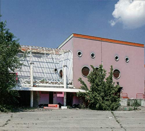 The image shows a pink building with a damaged roof and a parking lot. For accessibility purposes, a suitable alt text could be: "Damaged pink building with missing roof and parking lot."