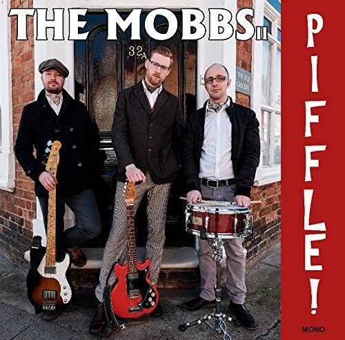 Three musicians with instruments stand in front of a brick building.
