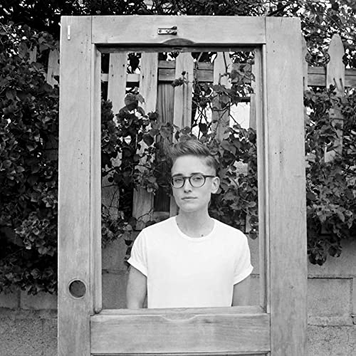 Black and white portrait of a person framed by a weathered wooden door.