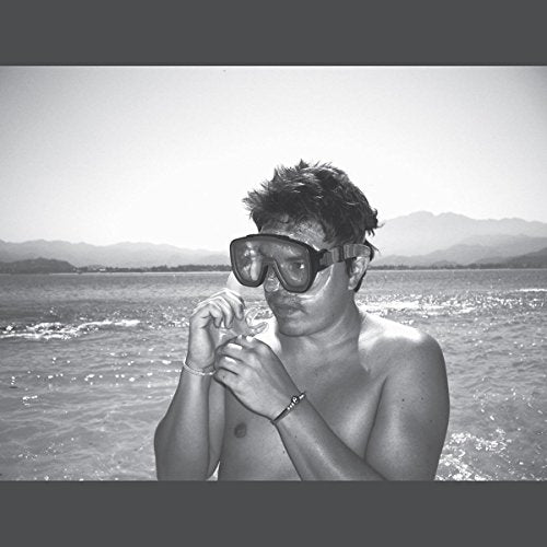 Black and white portrait of a shirtless man with diving goggles by the sea.