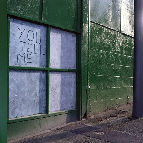 Green building with handwritten "You Tell Me" sign in a window.