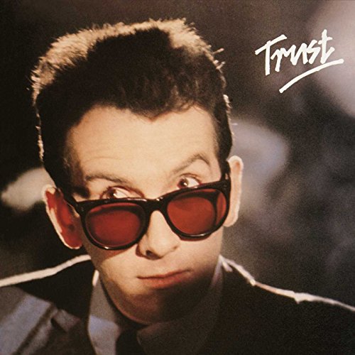 Record cover featuring Elvis Costello wearing dark sunglasses, close-up portrait.