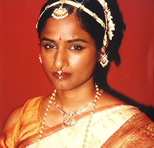 Priya Ragu portrait, adorned with traditional South Asian jewelry, red background.