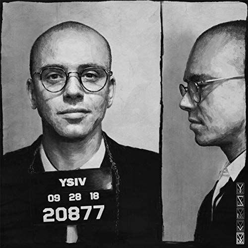 Black and white mugshot of a bald man wearing glasses and a suit.