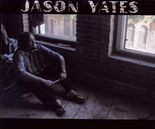 "Album cover with a man sitting on a dimly lit wooden floor."