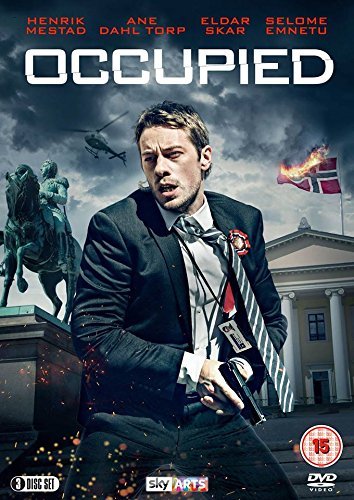 "Man in suit holding gun, with building and burning flag in the background."