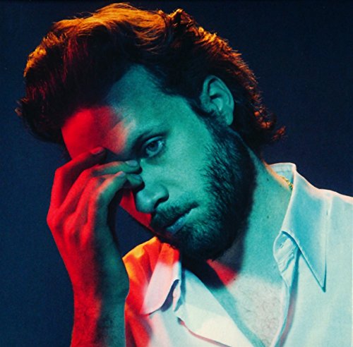 Father John Misty with a beard, hand to his forehead, lit by red and blue.