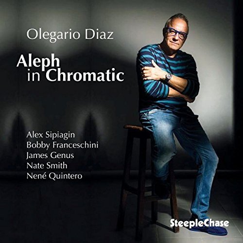 "Olegario Diaz sits on a stool, wearing a striped shirt and jeans."