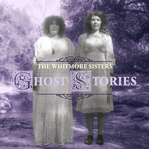 Two women in vintage dresses stand before a blurred forest backdrop.