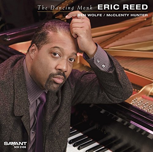 Man leaning on a piano with hand on head, wearing a suit.