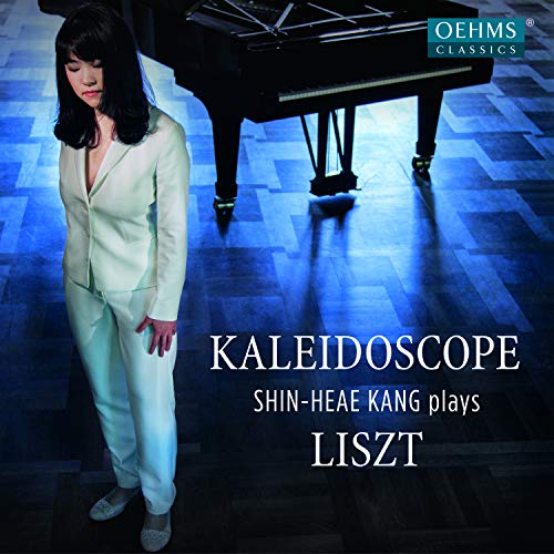 Shin Heae Kang in a white suit stands beside a grand piano.