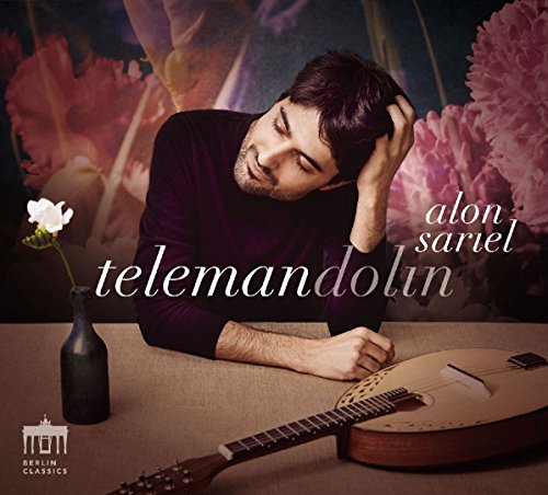 Man resting head on table beside mandolin and vase with white flower, pink floral background.