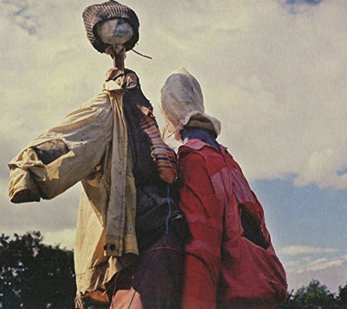 Two scarecrows with fabric heads stand in a field under a blue sky.