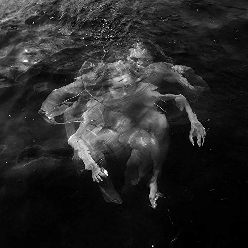 A black and white image of a person submerged underwater, surrounded by ripples and debris.