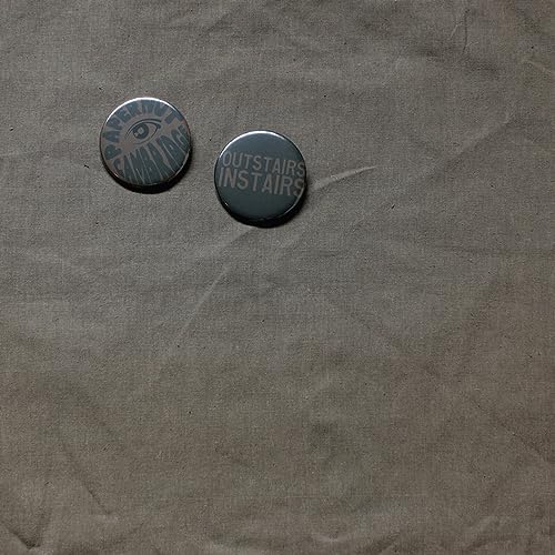 Two circular pins with text on a textured brown paper background.