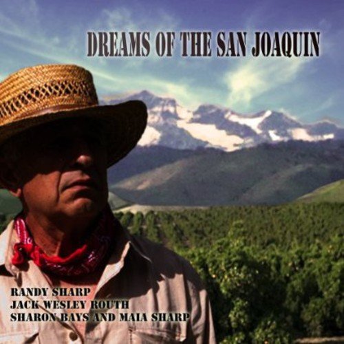 Man wearing straw hat and red bandana, mountains and trees in the background.