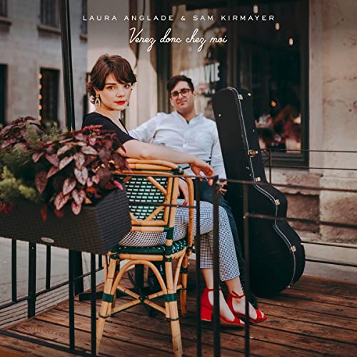 Two musicians pose with a guitar case on a cafe patio.