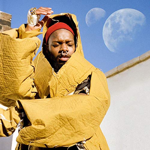 Serpentwithfeet in mustard-colored hooded garment, looking upwards at moons.