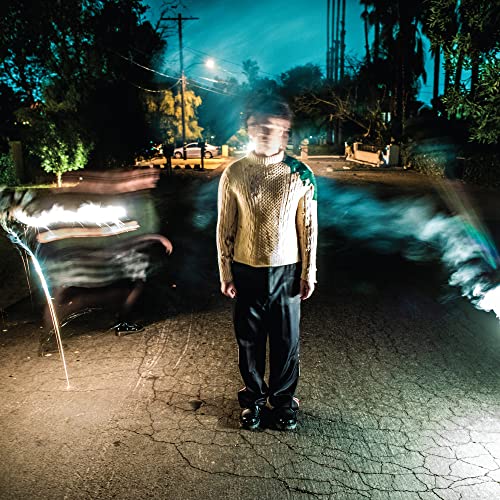 Person in sweater stands on a street at night, blurred lights.