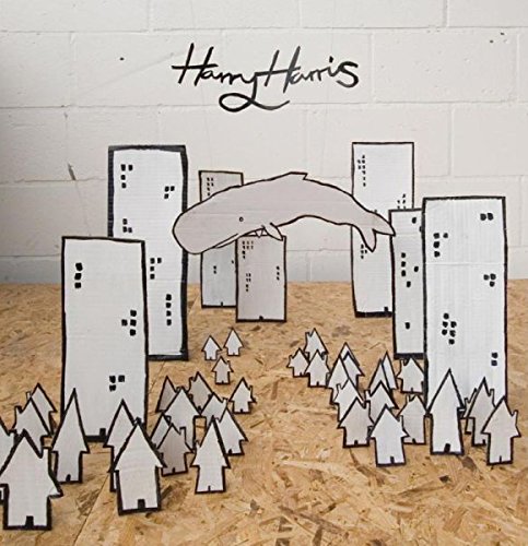 "Album cover featuring a whale over cardboard cityscape and trees, on a wooden surface."