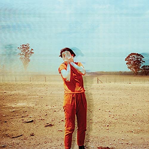 Person in orange suit covering eyes in a dusty field.