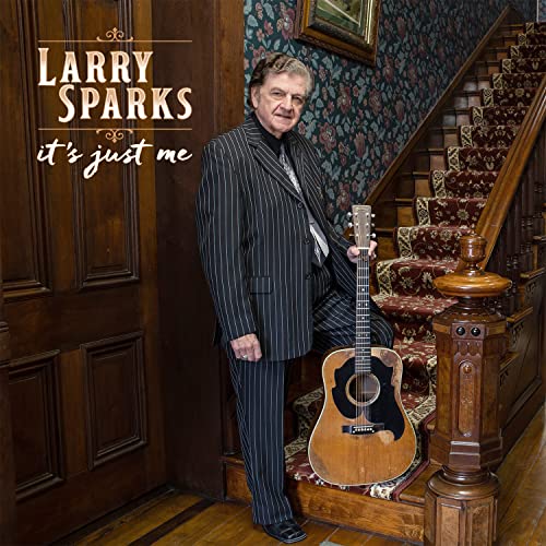 Larry Sparks in pinstripe suit holding an acoustic guitar on stairs.