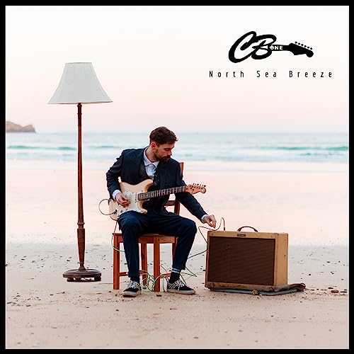 Man playing guitar on a beach with a lamp and amplifier.